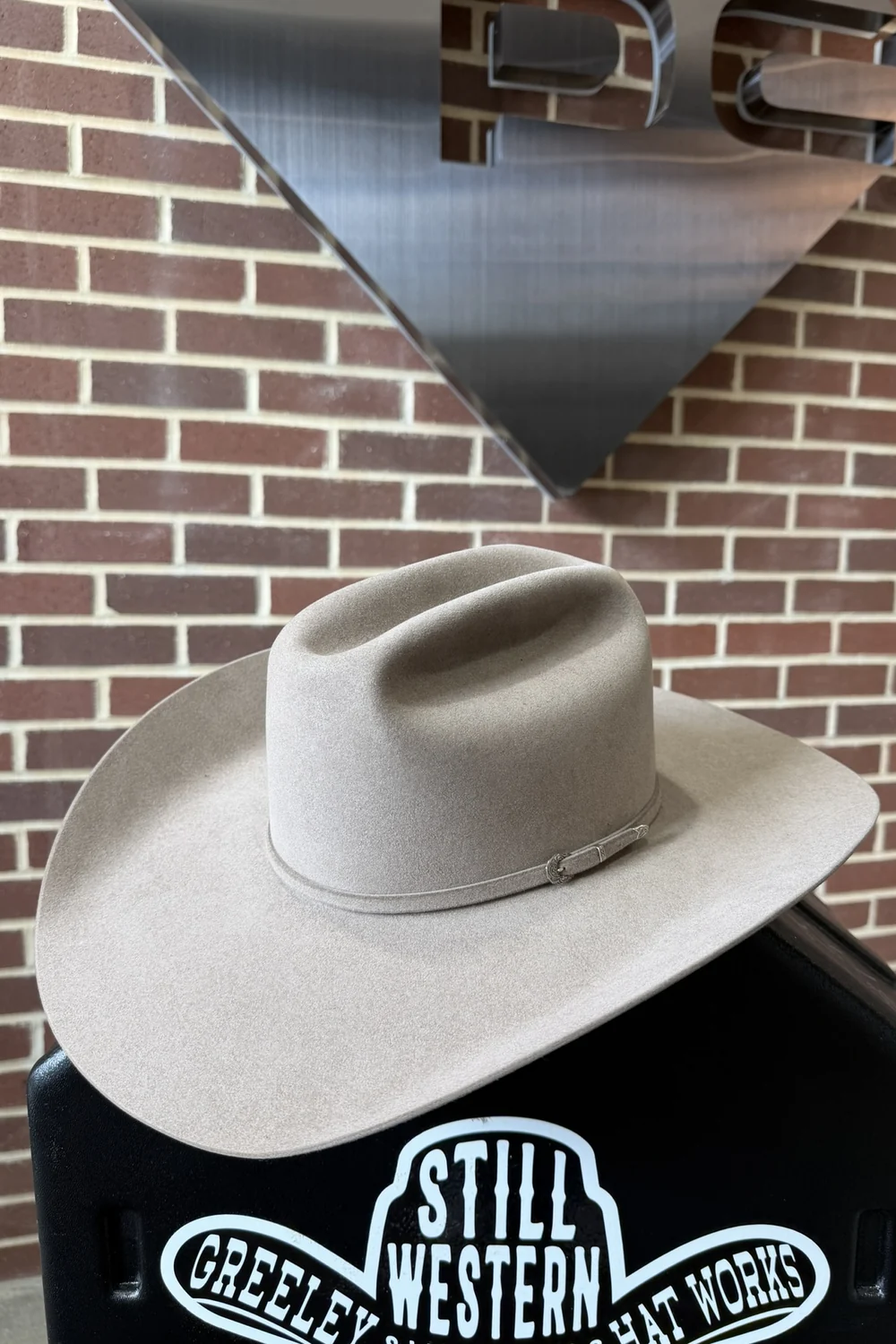 A Peoples Company cowboy hat resting on a stand beneath the PC diamond mounted on a brick wall