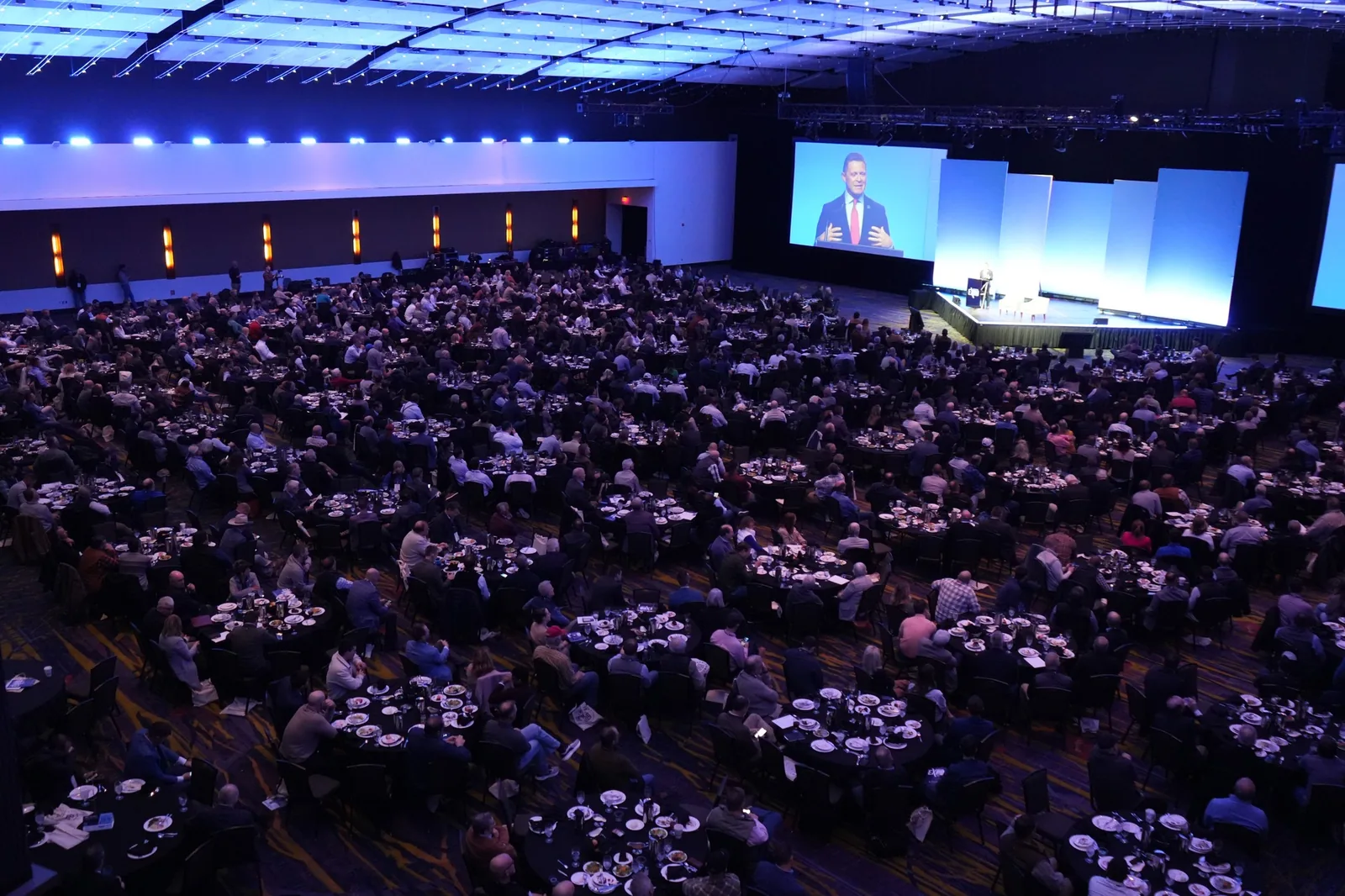 Attendees at round banquet tables fill a ballroom at the Land Investment Expo, facing a keynote speaker on stage